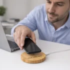 Man placing smartphone on a Rosedale Wireless Fast Charger beside a laptop on a desk.