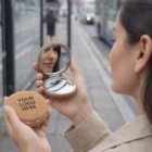 Woman with a Joliette Compact Mirrors checks her reflection at a bus stop.