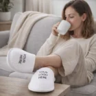 Woman relaxing, sipping from a mug in Chesterbrook Waffle Slippers with custom text.