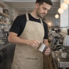 Barista wearing Pinafore Bib Aprons Elite in beige makes coffee with espresso machine in café.