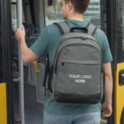 Man with gray Harlow Backpack boarding a yellow bus, YOUR LOGO HERE on the bag.