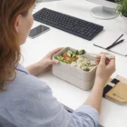 Savor salad and rice from Orena Stackable Lunch Boxes at your desk with keyboard and notepad.