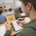 Student writing in an Argo Bamboo Note Pad with a wooden cover labeled YOUR LOGO HERE.