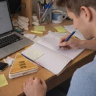 Man writing in notebook at desk with Maya Bamboo Clips and custom logo desk sign.