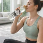 Woman in workout clothes drinks from a Grenda Glass Bottle With Bamboo Lid labeled Spread Kindness.