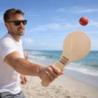 Man playing paddle ball on beach with Terra Paddle Ball Games; ocean and logo visible.
