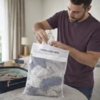Man puts clothes in Fleurieu Mesh Laundry Bags with custom logo beside a suitcase.