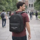 Man on campus wearing a Marion Springs Backpack with "YOUR LOGO HERE" text, walking outdoors.