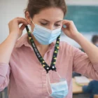 Woman attaches a face mask to an Elmour Max Mask Lanyard in a classroom.