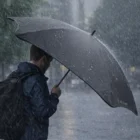 A person with a backpack holds a Blunt Sport Umbrella in heavy rain.