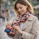Woman in beige coat smiles, adjusting a Brewton Custom Scarf with your logo displayed.