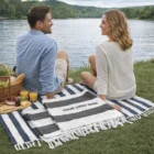 A couple picnics by a lake on a blanket, with Rustic Style Cotton Towels nearby.