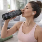 Woman in workout clothes with a Medina Screw Top Vacuum Bottle, wearing wireless earbuds.