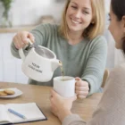 Woman pours chai from a 490Ml Stoneware Chai Teapot labeled "Your Logo Here" into a mug.