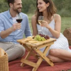 A smiling couple enjoys wine and snacks outdoors with Vistro Bamboo Folding Wine Tables.