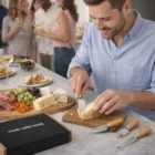 Man slicing cheese at a party with Keepsake Cheese Knife Sets in a gift box on the counter.