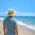 Person wearing a Rockville Wide Brim Hat stands on a sandy beach under a clear blue sky.