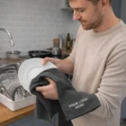 Man drying a plate with a dark Rochester Waffle Terry Towel in a kitchen.