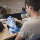 Man cleans laptop screen with blue cloth and Hale Magic Covers Large in a classroom.