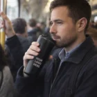 Bearded man drinks from a Brewpresso Coffee Press Vacuum Cup on a crowded subway.