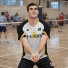 A male volleyball player in a Men’s Sublimated Tee Shirt gets ready to receive a serve in the gym.