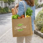 Person with fresh veggies, bananas, and bread in Corn Starch Jute Tote Bags on a city sidewalk.