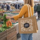 Woman holding carrots and a Natural Jute Handle Tote Bag at an outdoor farmers market.