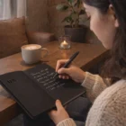 Someone writes in an Onyx Writing Set With Black Paper at a wooden table with coffee and a plant.