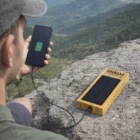 Man charging phone with a Bamboo Solar Power Banks Aus 10,000mAh on a rocky mountain overlook.