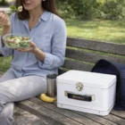 Woman eating salad on a park bench with her Snackcrate Tin Lunch Box, thermos, and banana.