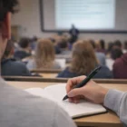 Student takes notes with Shiny Gunmetal Ballpoint Pens during a crowded classroom lecture.