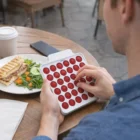 Someone uses a Zapcube Fidget Popper Board at an outdoor table with food and coffee.