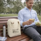 Man eating lunch on a bench with salad, sandwich, water, and an Insulated Cotton Canvas Lunch Bag.