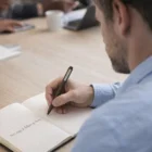 Man jotting next steps with Coffee Grind Blend Eco Ball Pens, notebook by his side at meeting.