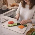 Woman slices cucumber on BPA-Free Chopping Boards with tomatoes, carrots, and broccoli nearby.