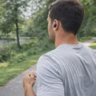Man runs on park path wearing Skullcandy TWS Earbuds and a light gray shirt.