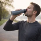 Man outdoors drinking from a 700Ml Aluminium Bottle, wearing a dark long-sleeve shirt.