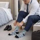 Man in suit puts on Full Colour Sublimated Crew Socks while sitting, shoes beside him.