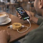 Person charges phone with Bamboo Charging Cables at cafe table beside a coffee cup.