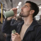 Man drinks from a 650Ml Glass Bottle on a crowded subway train.