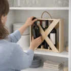 Person placing a wine bottle into Triple Wine Crates on a kitchen shelf near dishes.
