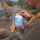 Man outdoors opens a Travel Compressed Towels pouch next to his camping stove.