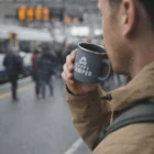 Man holding a 500Ml Matte Enamel Mug, standing by a busy street with blurred people behind.