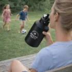 Woman enjoying a 2L Vacuum Bottle while watching kids play soccer on the grass.