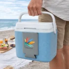 Person holding Slim Design Can Cooler on the beach with a picnic setup in the background.