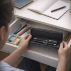 Person holding a Leather-Like Pen Case by a desk with stationery and an open notebook.
