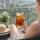 Woman enjoys iced tea in Elegant Deco Glasses on a balcony with outdoor seating.