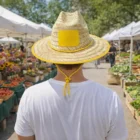 Person in Classic Straw Hats at outdoor market with flowers and produce on a sunny day.