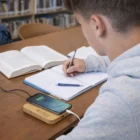 Student writing in notebook with phone on a 15W Bamboo Charging Hub at the library table.