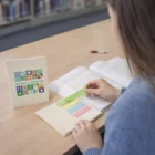 A woman uses an Eco-Friendly Spirit Sticky Note Booklet to mark a textbook at the library.